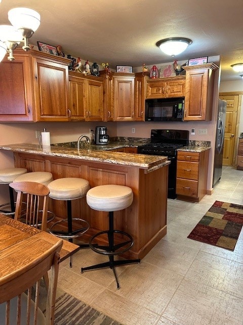 kitchen featuring kitchen peninsula, light stone countertops, black appliances, and a breakfast bar