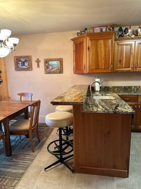 kitchen featuring sink, a breakfast bar, an inviting chandelier, and dark stone counters