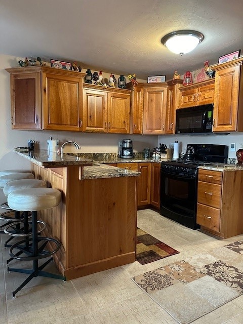 kitchen featuring black appliances, kitchen peninsula, dark stone counters, and a breakfast bar