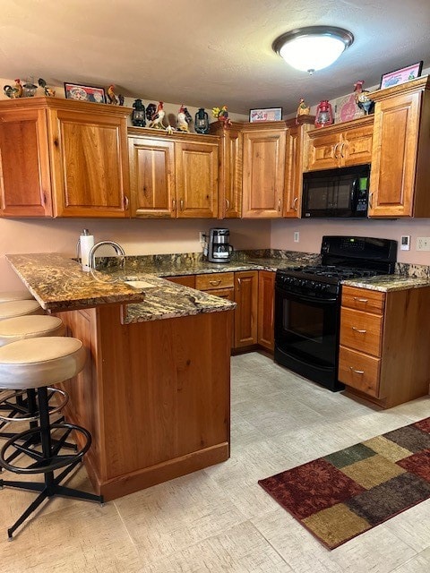 kitchen featuring kitchen peninsula, a kitchen bar, dark stone countertops, black appliances, and sink