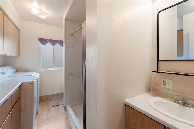 bathroom with tiled shower, wood-type flooring, washing machine and dryer, and vanity