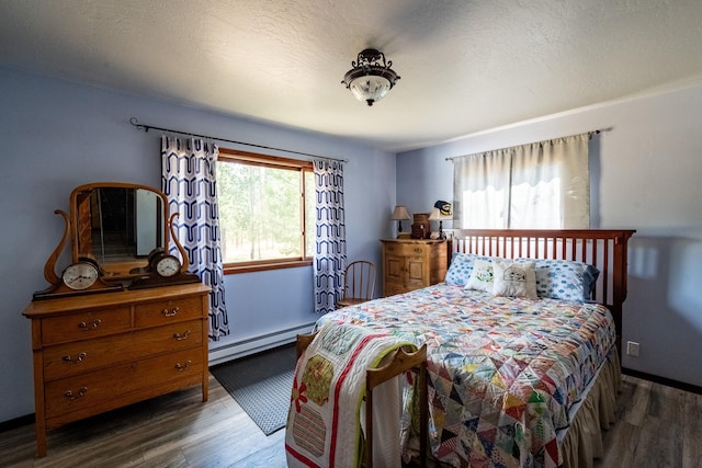bedroom featuring a textured ceiling, a baseboard heating unit, and wood finished floors