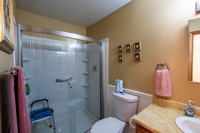 bathroom with wainscoting, vanity, a shower stall, and toilet