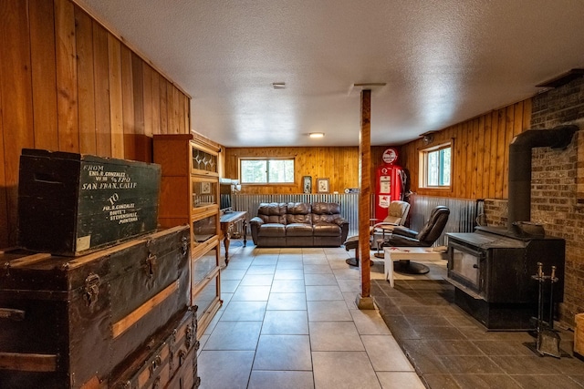 tiled living area featuring wooden walls, a wood stove, and a textured ceiling
