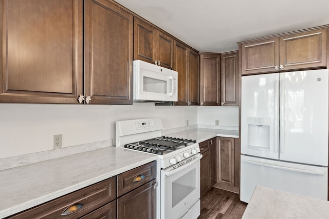 kitchen with dark brown cabinetry, dark wood-type flooring, and white appliances