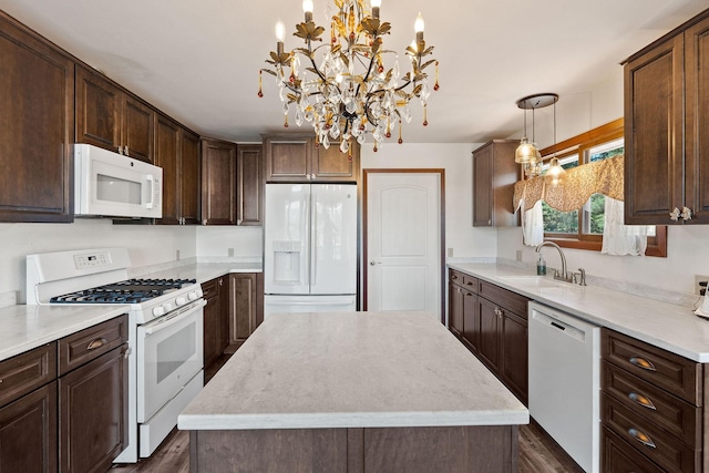 kitchen featuring white appliances, a sink, hanging light fixtures, light countertops, and a center island