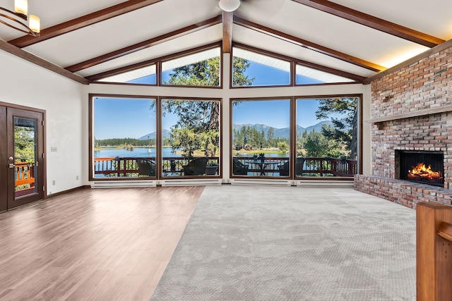 unfurnished living room with wood-type flooring, vaulted ceiling with beams, a water view, brick wall, and a brick fireplace