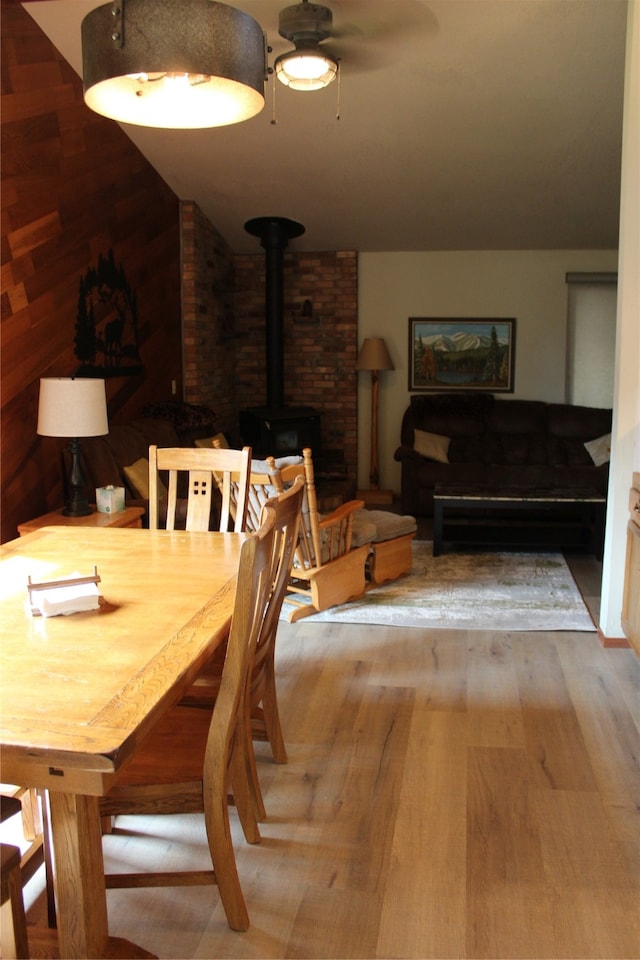 dining room featuring a wood stove, ceiling fan, light hardwood / wood-style floors, brick wall, and vaulted ceiling