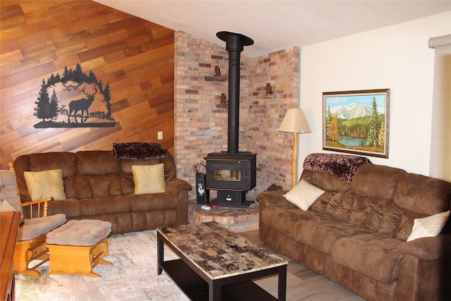 living room with wooden walls, a wood stove, lofted ceiling, brick wall, and hardwood / wood-style flooring