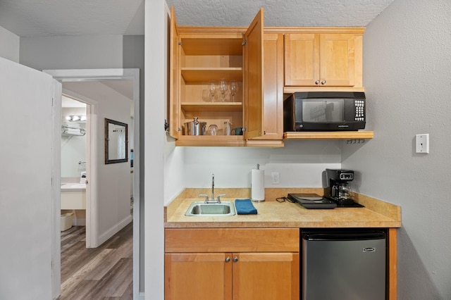 kitchen featuring light countertops, wood finished floors, a sink, black microwave, and refrigerator