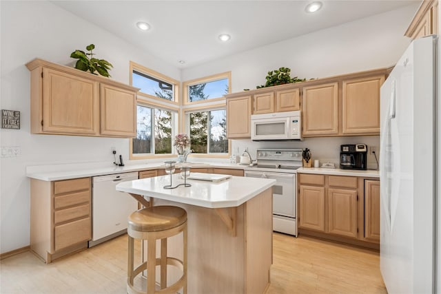 kitchen with a kitchen breakfast bar, light countertops, light brown cabinets, and white appliances