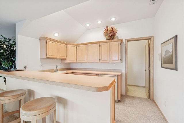 kitchen featuring light countertops, light carpet, a sink, a kitchen breakfast bar, and light brown cabinetry