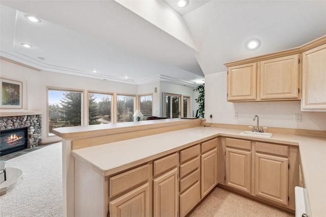kitchen featuring light countertops, a peninsula, a sink, open floor plan, and light brown cabinetry
