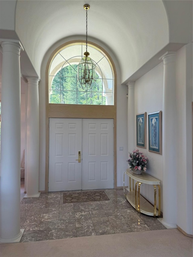 entryway featuring a towering ceiling, a chandelier, and decorative columns