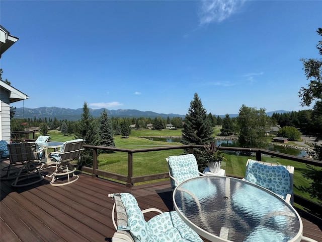 wooden deck featuring a lawn, a mountain view, and outdoor dining space