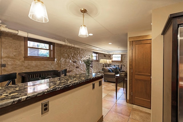 kitchen featuring decorative light fixtures, tasteful backsplash, open floor plan, dark stone counters, and light tile patterned floors