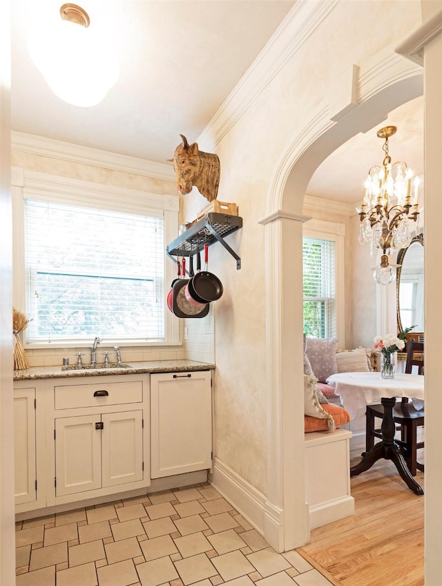 kitchen with crown molding, light stone countertops, arched walkways, white cabinetry, and a sink