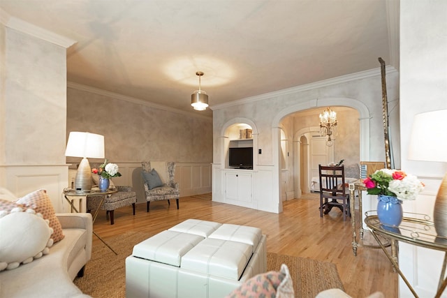 living room featuring arched walkways, a decorative wall, crown molding, and light wood-type flooring