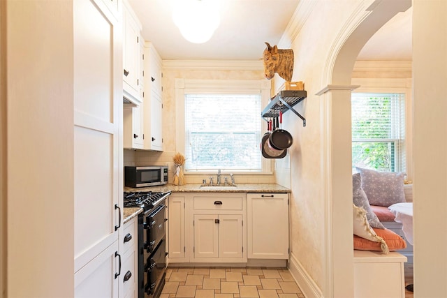 kitchen featuring stainless steel microwave, crown molding, arched walkways, gas stove, and a sink