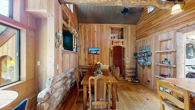 dining room with wood-type flooring, stacked washer and clothes dryer, and wooden walls