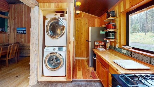 clothes washing area featuring stacked washer / drying machine, wooden walls, and light wood-type flooring