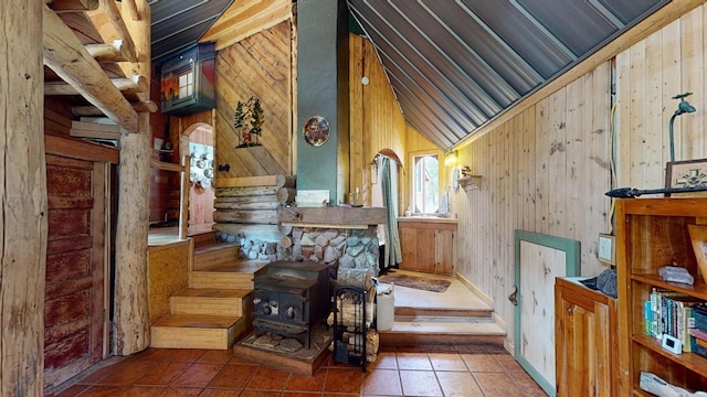 staircase with lofted ceiling, wooden walls, tile patterned floors, and a wood stove