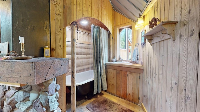 bathroom featuring vaulted ceiling, sink, and wood walls