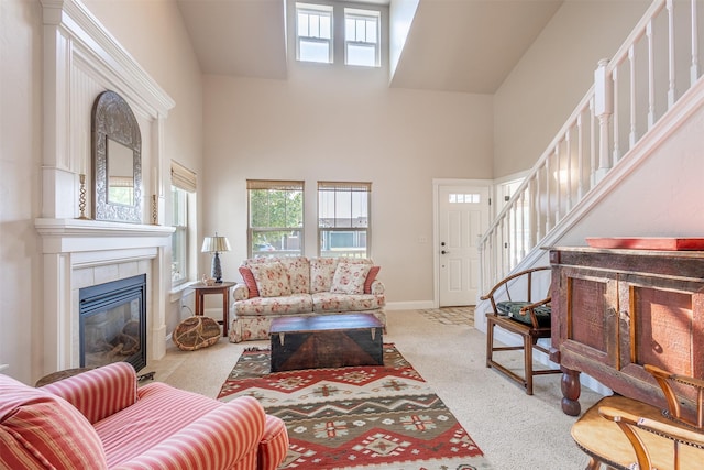 carpeted living area with stairway, a tile fireplace, a high ceiling, and baseboards