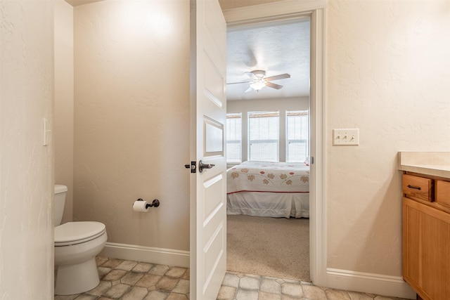 bathroom featuring baseboards, toilet, vanity, and a textured wall