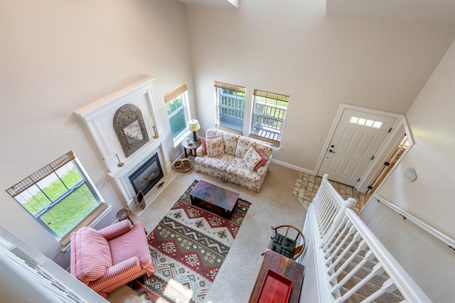 carpeted living area featuring a fireplace with flush hearth, baseboards, stairs, and a towering ceiling