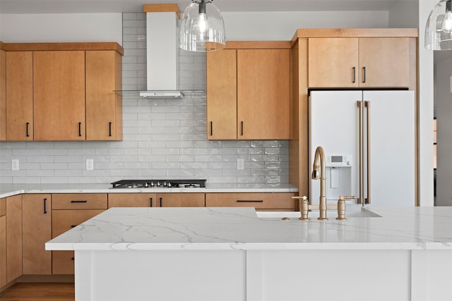 kitchen with tasteful backsplash, light hardwood / wood-style floors, high end white fridge, wall chimney range hood, and stainless steel gas stovetop