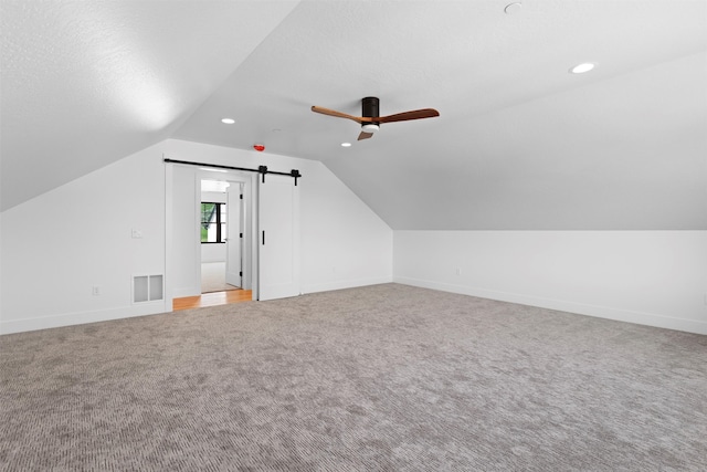 bonus room featuring ceiling fan, a barn door, light carpet, and lofted ceiling