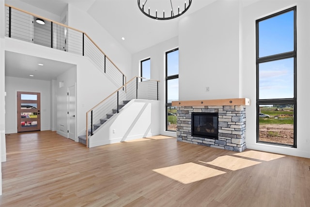 unfurnished living room with a towering ceiling, a fireplace, light wood-type flooring, and an inviting chandelier