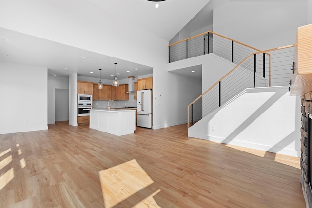 unfurnished living room featuring a towering ceiling, a stone fireplace, sink, and light hardwood / wood-style floors