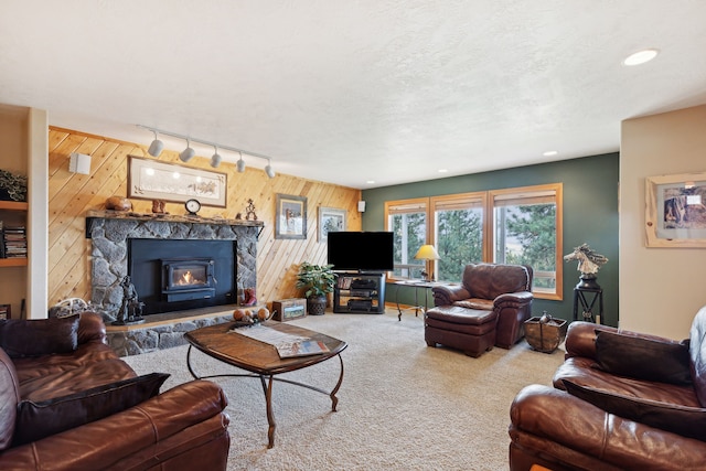 living room with a textured ceiling, a stone fireplace, carpet flooring, wooden walls, and rail lighting