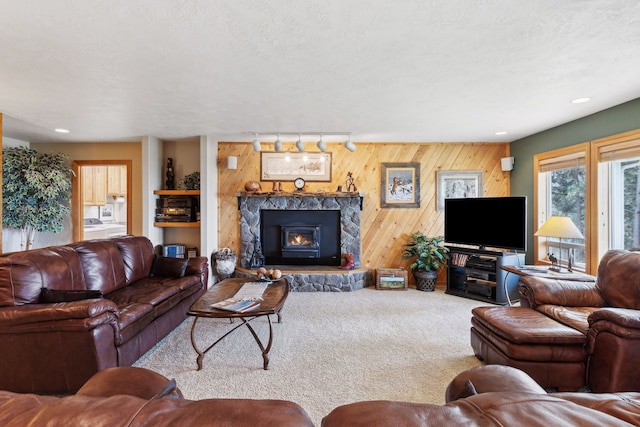 living room with a textured ceiling, a stone fireplace, wooden walls, carpet, and track lighting