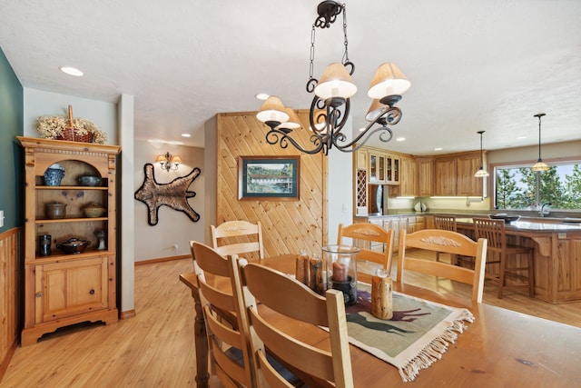 dining area with wood walls, a notable chandelier, and light wood-type flooring