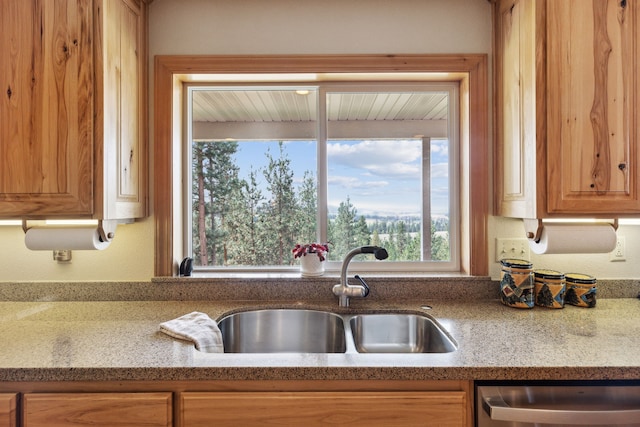 kitchen with stainless steel dishwasher, sink, and light stone countertops