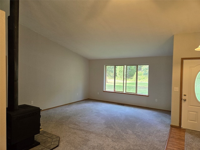 unfurnished living room featuring light colored carpet, a wood stove, and lofted ceiling