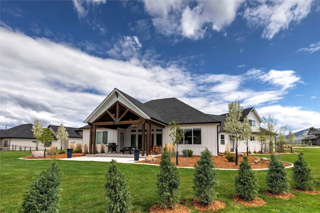 back of property with a patio, fence, a yard, a shingled roof, and board and batten siding