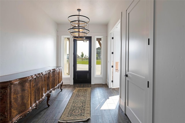 entrance foyer with an inviting chandelier, dark wood-style floors, and a wainscoted wall