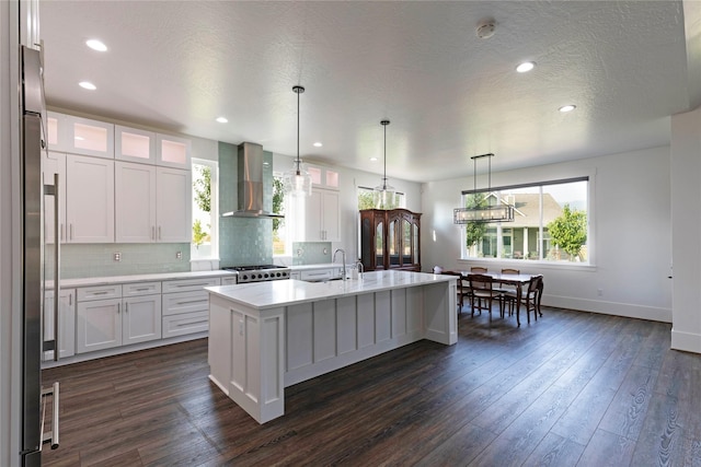 kitchen featuring dark wood-style floors, decorative backsplash, light countertops, stove, and wall chimney range hood