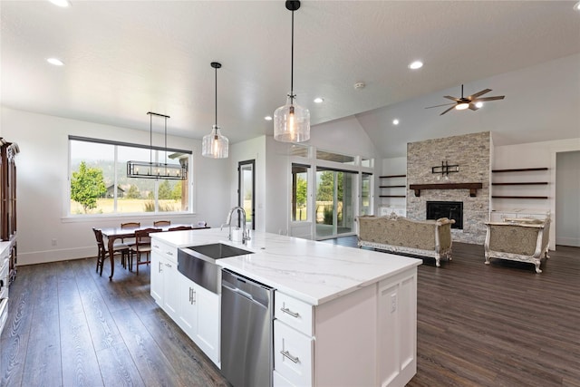 kitchen with dark wood-type flooring, a kitchen island with sink, a sink, a stone fireplace, and dishwasher