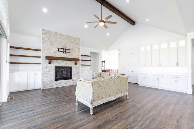 unfurnished living room with high vaulted ceiling, beam ceiling, ceiling fan, a stone fireplace, and dark wood-type flooring