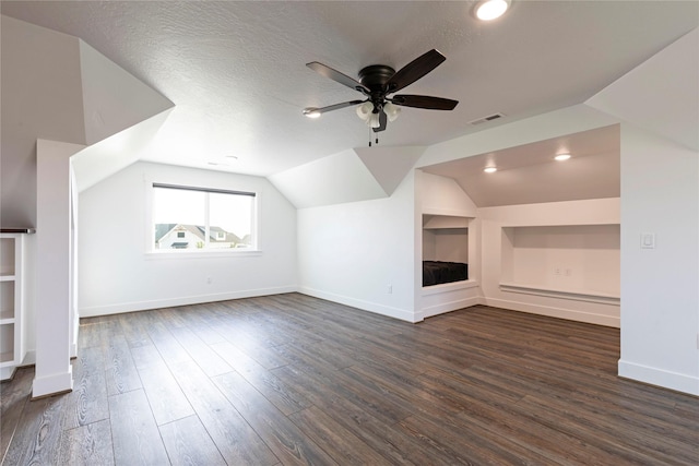 additional living space featuring visible vents, lofted ceiling, dark wood-style flooring, ceiling fan, and a textured ceiling