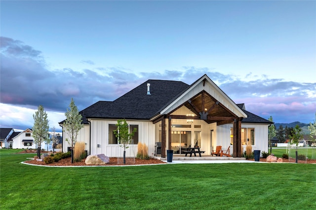 back of property with a patio area, a lawn, board and batten siding, and roof with shingles