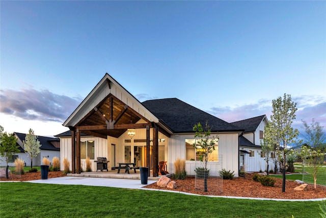 back of property with a patio, a lawn, board and batten siding, and a shingled roof