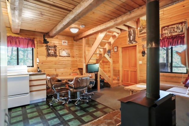 office space with beamed ceiling, wooden walls, carpet floors, and a wood stove