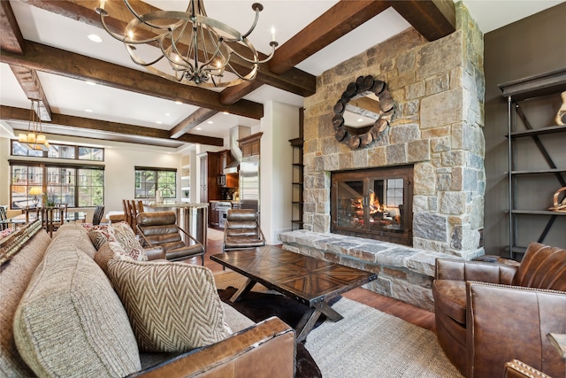 living room with beam ceiling, a stone fireplace, hardwood / wood-style floors, and a chandelier