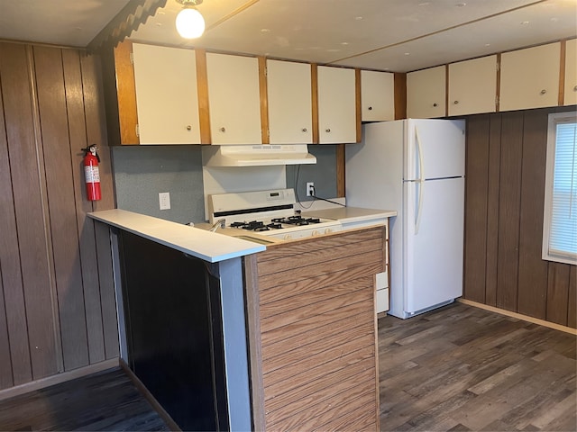 kitchen with dark hardwood / wood-style flooring, cream cabinets, wooden walls, white fridge, and range